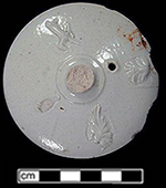 Lid to teapot or coffee pot with sprig molded decorations. The slight shadow created by the metal sprig mold can be seen around the sprigged element at the lower right and in the detail shot. The unglazed area at the lower left is where another sprigged element detached from the lid., Vessel 224, recovered from 1740s level within a well filled c. 1720s-1750s - 18PR175.